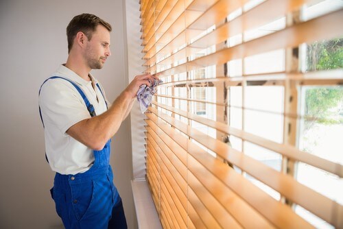 man in coveralls cleaning faux wood blinds with rag